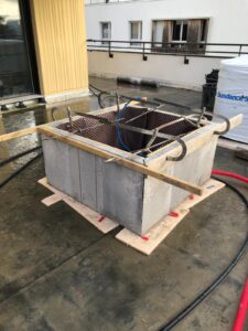 Construction d'un bac béton sur terrasse, avec coffrage, armatures métalliques et drainage alvéolaire visible. Mention Sundance Spas.