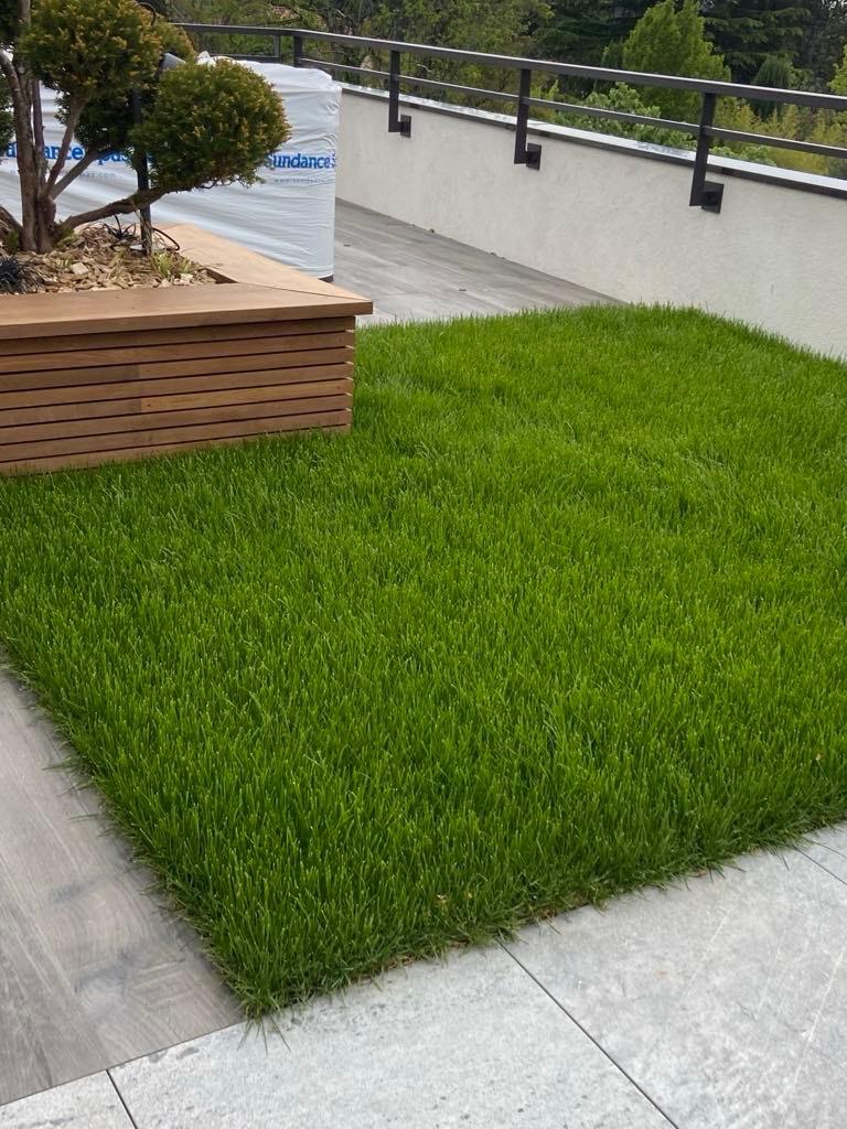 Pelouse de gazon vert vif sur une terrasse moderne avec jardinière en bois, balustrade noire et emballage blanc « sundance ».